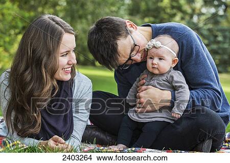 Picture - A married couple with a baby daughter in a park; Edmonton, Alberta, Canada. Fotosearch