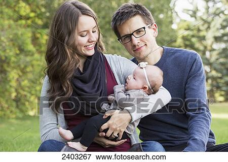 Stock Photo - A married couple with a baby daughter in a park; Edmonton, Alberta, Canada. Fotosearch