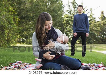 Stock Photograph - A married couple with a baby daughter in a park; Edmonton, Alberta, Canada. Fotosearch