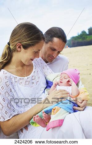 Stock Photograph - A mother and father with their newborn daughter on the beach; Kauai, Hawaii, United States of America. Fotosearch