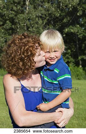A mother holds her young son and kisses him on his cheek; Stony Plain, Alberta, Canada View Large Photo Image Picture - A mother holds her young son and kisses him on his cheek; Stony Plain, Alberta, Canada. Fotosearch