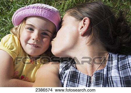 Picture - A mother kisses her daughter while laying on the grass together; Toronto, Ontario, Canada. Fotosearch