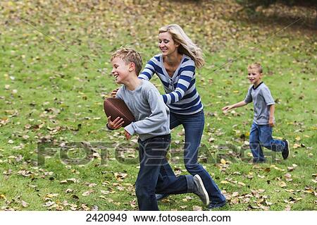 Stock Photo - A mother playing football with her sons in a park during autumn; Edmonton, Alberta, Canada. Fotosearch