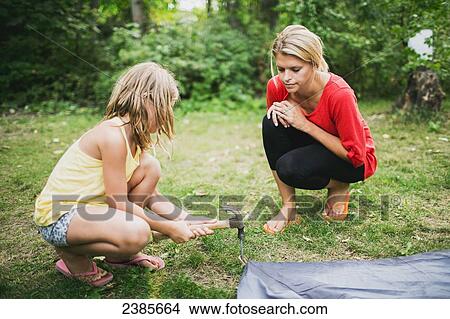 Picture - A mother watches her daughter hammer in a tent peg; Peachland, British Columbia, Canada. Fotosearch