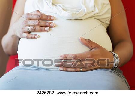 Stock Image - A pregnant mother putting hands on her belly; Toronto, Ontario, Canada. Fotosearch