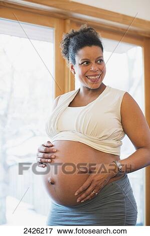 A pregnant woman holds her bare belly at the end of pregnancy in the window light; Toronto, Ontario, Canada View Large Photo Image Stock Photo - A pregnant woman holds her bare belly at the end of pregnancy in the window light; Toronto, Ontario, Canada. Fotosearch