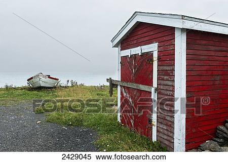 Stock Photography - A red weathered shed and a boat on the shore at the coast; Sally's Cove, Newfoundland, Canada. Fotosearch