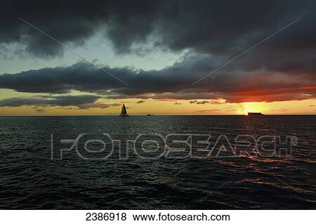 A sailboat on the ocean water off the coast of Waikiki at sunset; Waikiki, Oahu, Hawaii, United States of America View Large Photo Image Stock Photo - A sailboat on the ocean water off the coast of Waikiki at sunset; Waikiki, Oahu, Hawaii, United States of America. Fotosearch