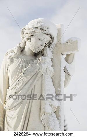 A tombstone with a sculpture of a girl holding a cross in Burnsland Cemetery in winter; Calgary, Alberta, Canada View Large Photo Image Picture - A tombstone with a sculpture of a girl holding a cross in Burnsland Cemetery in winter; Calgary, Alberta, Canada. Fotosearch