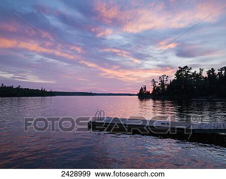 Stock Photo - A tranquil lake reflecting the pink clouds of a sunset; Ontario, Canada. Fotosearch