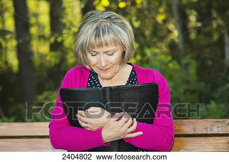 Stock Image - A woman embracing her open Bible on a park bench; Edmonton, Alberta, Canada. Fotosearch