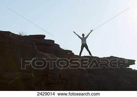 A woman stands on a rock ledge with arms raised in celebration; Prince Edward Island, Canada View Large Photo Image Picture - A woman stands on a rock ledge with arms raised in celebration; Prince Edward Island, Canada. Fotosearch