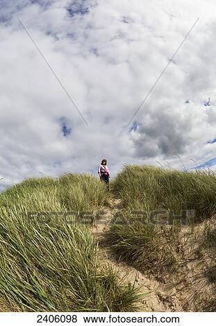 A woman stands under a cloudy sky at the top of a sand dune covered in tall grass; Northumberland, England View Large Photo Image Stock Photo - A woman stands under a cloudy sky at the top of a sand dune covered in tall grass; Northumberland, England. Fotosearch