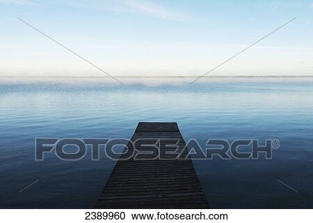 Stock Image - A wooden dock leading out to a misty tranquil lake in Riding Mountain National Park; Wasagaming, Manitoba, Canada. Fotosearch