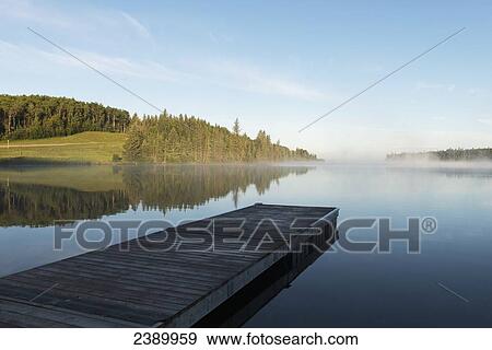 A wooden dock leading out to a misty tranquil lake in Riding Mountain National Park; Wasagaming, Manitoba, Canada View Large Photo Image Stock Photo - A wooden dock leading out to a misty tranquil lake in Riding Mountain National Park; Wasagaming, Manitoba, Canada. Fotosearch