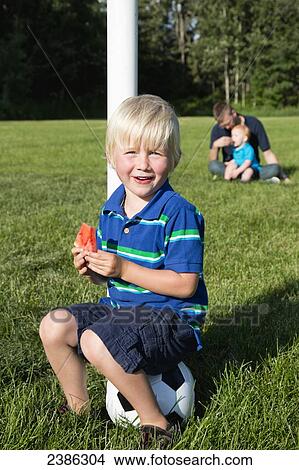 A young boys sits on a soccer ball eating a piece of watermelon in a park; Stony Plain, Alberta, Canada View Large Photo Image Picture - A young boys sits on a soccer ball eating a piece of watermelon in a park; Stony Plain, Alberta, Canada. Fotosearch