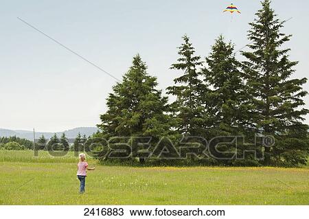Stock Image - A young girl flying her kite over a field of wildflowers; Thunder Bay, Ontario, Canada. Fotosearch