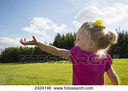 Stock Photograph - A young girl reaching up to the sky in a park; St. Albert, Alberta, Canada. Fotosearch