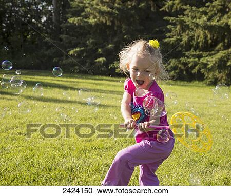 Stock Image - A young girl running in a park making bubbles; St. Albert, Alberta, Canada. Fotosearch