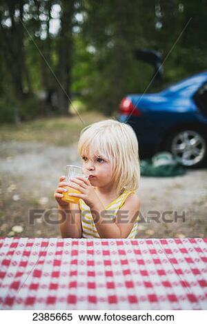 Stock Photography - A young girl sits at a picnic table drinking; Peachland, British Columbia, Canada. Fotosearch