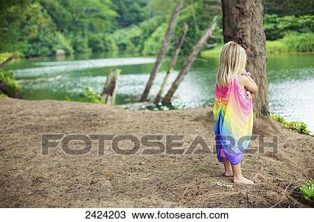 Stock Image - A young girl stands on the beach at the water's edge; Kauai, Hawaii, United States of America. Fotosearch