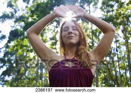 Stock Photo - A young woman holding her hands up above her head encasing the sunlight; Hawaii, United States of America. Fotosearch