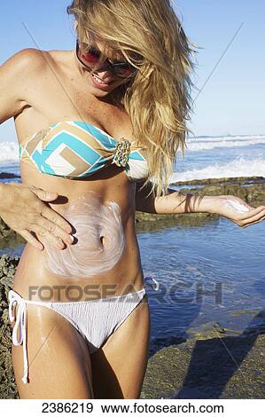 A young woman in a bikini applying sunscreen at the water's edge; Hawaii, United States of America View Large Photo Image Stock Photo - A young woman in a bikini applying sunscreen at the water's edge; Hawaii, United States of America. Fotosearch