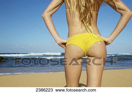 Stock Image - A young woman in a yellow bikini stands on the beach looking out at the ocean; Kauai, Hawaii, United States of America. Fotosearch