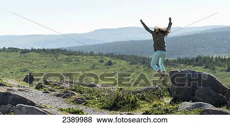 A young woman jumps from a rock with arms in the air; St. John's, Newfoundland and Labrador, Canada View Large Photo Image Stock Photo - A young woman jumps from a rock with arms in the air; St. John's, Newfoundland and Labrador, Canada. Fotosearch