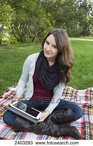 A young woman sitting in a park using a tablet; Edmonton, Alberta, Canada View Large Photo Image Stock Image - A young woman sitting in a park using a tablet; Edmonton, Alberta, Canada. Fotosearch