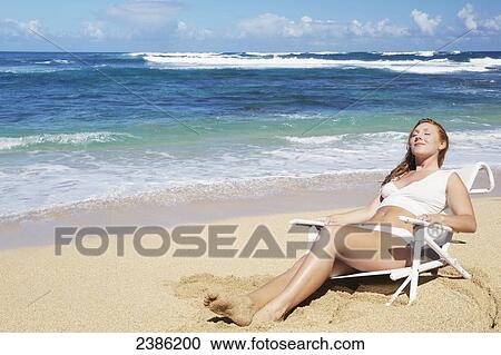Stock Image - A young woman sunbathing on the beach; Kauai, Hawaii, United States of America. Fotosearch