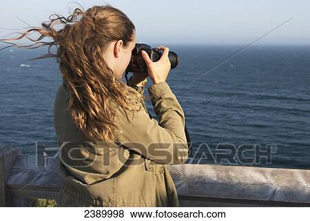 A young woman takes a photograph at the coast of the Atlantic Ocean; Port Rexton, Newfoundland and Labrador, Canada View Large Photo Image Stock Photo - A young woman takes a photograph at the coast of the Atlantic Ocean; Port Rexton, Newfoundland and Labrador, Canada. Fotosearch