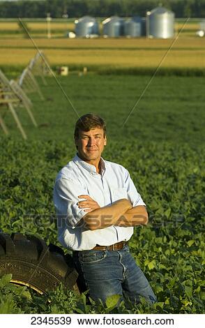 Agriculture - A farmer poses while sitting on the tire of a center pivot irrigation system in his mid growth soybean field / near Hoffman, Minnesota, USA. View Large Photo Image Stock Photo - Agriculture - A farmer poses while sitting on the tire of a center pivot irrigation system in his mid growth soybean field / near Hoffman, Minnesota, USA.. Fotosearch