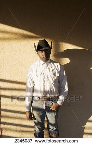 Agriculture - A young black cowboy stands against a bunkhouse wall with late afternoon shadows / Childress, Texas, USA. View Large Photo Image Stock Photo - Agriculture - A young black cowboy stands against a bunkhouse wall with late afternoon shadows / Childress, Texas, USA.. Fotosearch