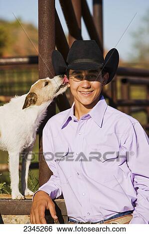 Agriculture - A young cowboy poses while his dog licks his ear / Childress, Texas, USA. View Large Photo Image Stock Photograph - Agriculture - A young cowboy poses while his dog licks his ear / Childress, Texas, USA.. Fotosearch