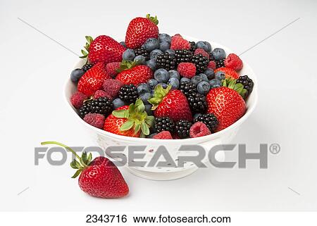 Stock Photograph - Agriculture - Fresh strawberries, red raspberries, blackberries and blueberries in a colander on a white surface.. Fotosearch