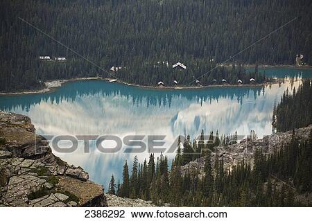 Stock Image - Alpine lake framed by shoreline and mountain cliffs and reflecting the mountains; British Columbia, Canada. Fotosearch