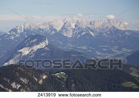 Alpine village on grassy rolling meadows with snow covered mountain range in the distance with blue sky and clouds; Alpbach, Austria View Large Photo Image Stock Photo - Alpine village on grassy rolling meadows with snow covered mountain range in the distance with blue sky and clouds; Alpbach, Austria. Fotosearch