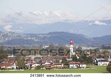Alpine village with church steeple and rolling hills with snow covered mountains in the background; Radfield, Austria View Large Photo Image Stock Image - Alpine village with church steeple and rolling hills with snow covered mountains in the background; Radfield, Austria. Fotosearch