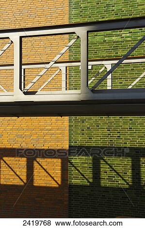 Stock Photo - An elevated walkway with a brick wall behind it in two colours, brown and green; Hamburg, Germany. Fotosearch