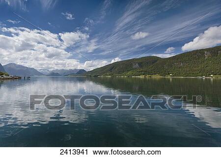 Blue sky and cloud reflected in tranquil water with forested mountains along the shoreline; Andalsnes, Rauma, Norway View Large Photo Image Stock Image - Blue sky and cloud reflected in tranquil water with forested mountains along the shoreline; Andalsnes, Rauma, Norway. Fotosearch