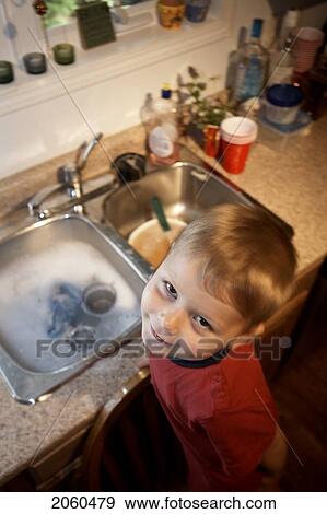 Stock Photo - Boy Standing On Chair At Kitchen Sink Washing Dishes. Fotosearch