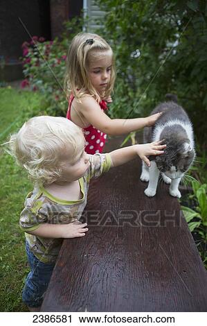 Stock Image - Brother and sister pet their cat outside in the garden; Toronto, Ontario, Canada. Fotosearch