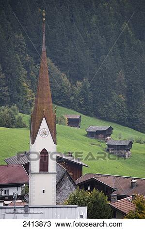 Church steeple in village with grassy slope meadow, wooden barns and treed mountain slope in the background; Lanserbach, Austria View Large Photo Image Stock Image - Church steeple in village with grassy slope meadow, wooden barns and treed mountain slope in the background; Lanserbach, Austria. Fotosearch