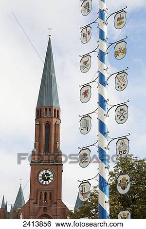 Stock Photograph - Close up of a traditional bavarian may pole with blue and white stripes with crests and a church steeple in the background; Munich, Germany. Fotosearch