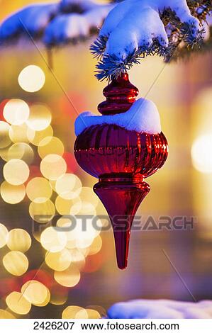 Close up of red Christmas ornament at night hanging on a snow covered evergreen tree with blurred Christmas lights in the background View Large Photo Image Stock Photo - Close up of red Christmas ornament at night hanging on a snow covered evergreen tree with blurred Christmas lights in the background. Fotosearch