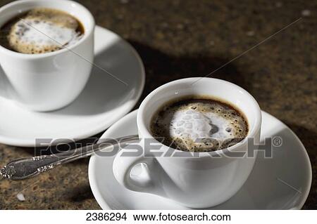 Picture - Close up of two espresso coffee cups and saucers with foam and coffee on granite counter; Calgary, Alberta, Canada. Fotosearch