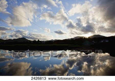 Stock Image - Clouds and blue sky reflected in the tranquil water of Sneem Harbour; Sneem, County Kerry, Ireland. Fotosearch