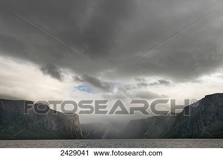 Stock Image - Clouds and rainfall over the cliffs in Norris Point, Gros Morne National Park; Newfoundland, Canada. Fotosearch