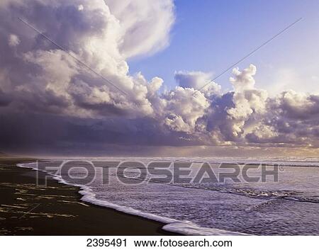 Stock Image - Clouds and tide moving onto the shore along the beach; Winchester Bay, Oregon, United States of America. Fotosearch
